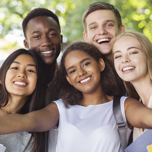 Cheerful international friends teenagers taking selfie while walking in summer park, happy memories concept